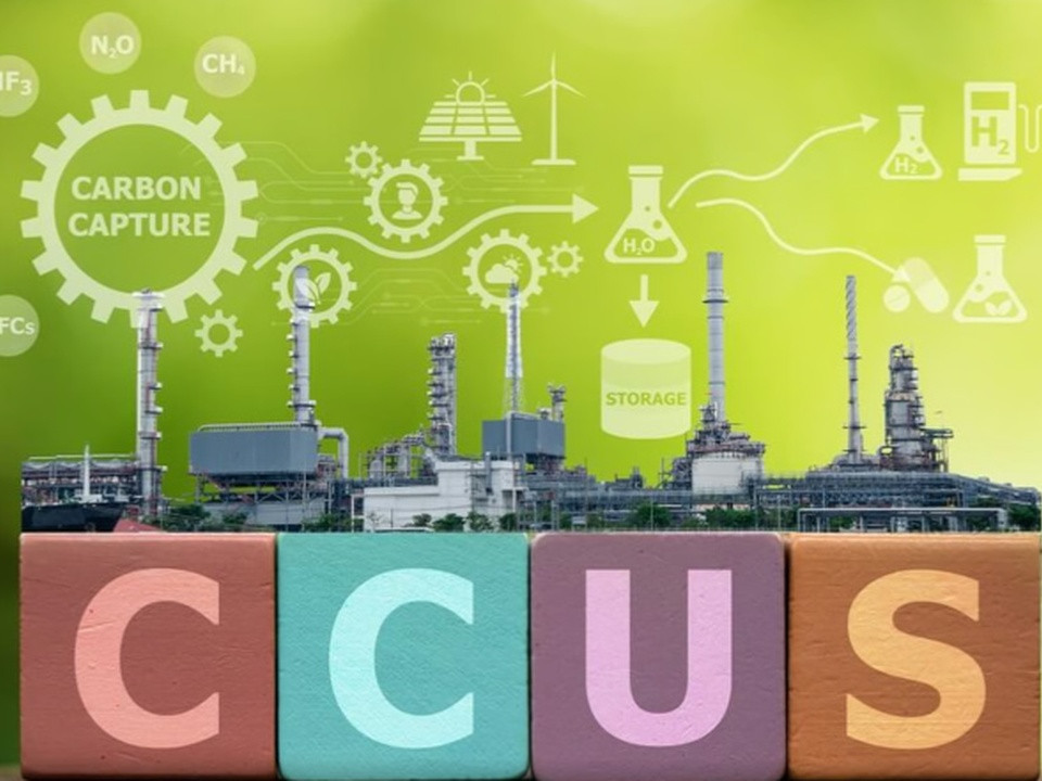 Industrial plant with colorful blocks spelling CCUS in the foreground and a carbon capture diagram in a green background, illustrating CCUS technology concept.